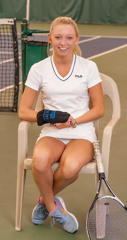 Photo of a woman sitting in a chair on a tennis court with  a wrap on her hand 