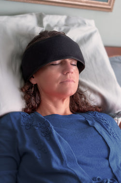  Women laying in bed with a black wrap around her forehead 